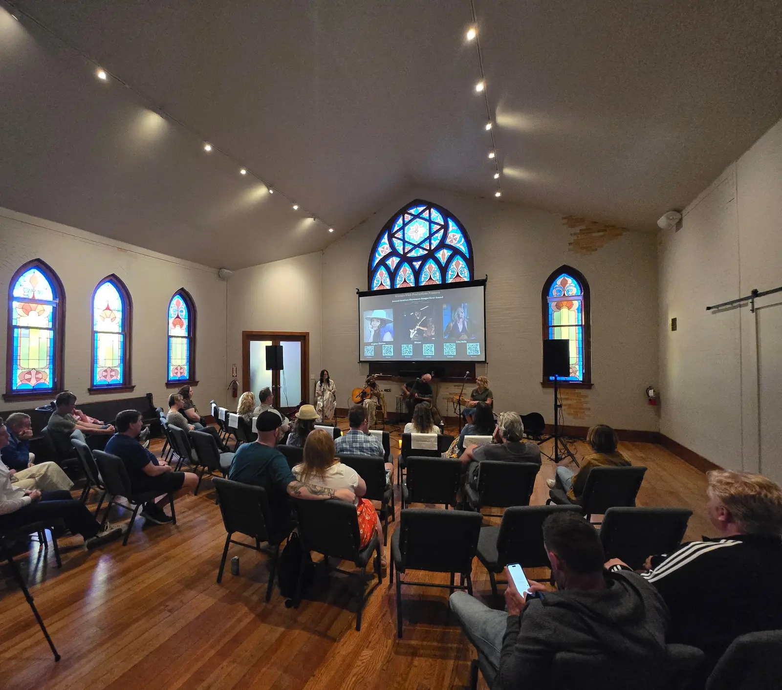 An audience watches an acoustic set beneath the stained-glass rose window