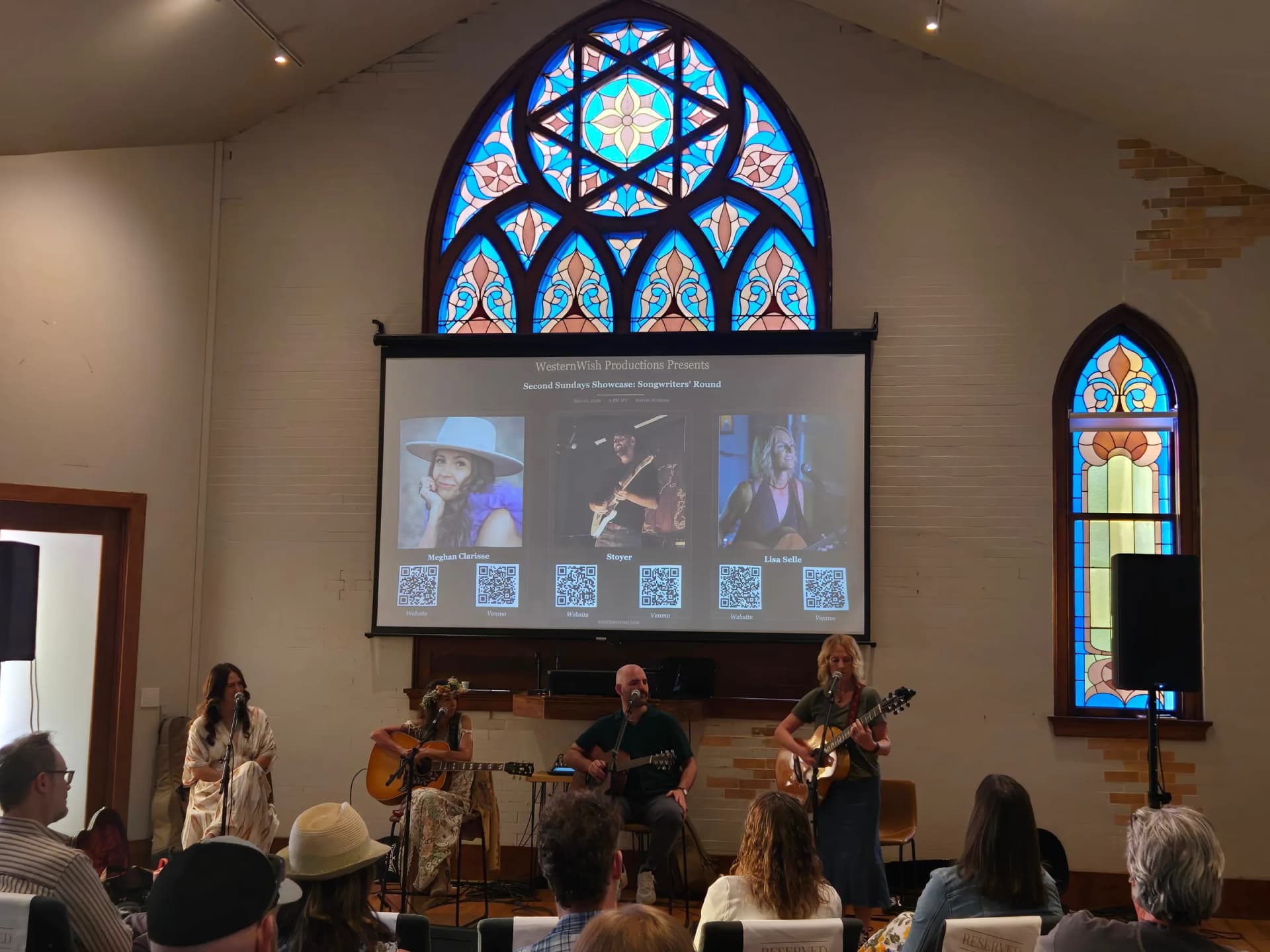 Four musicians perform a songwriters' round beneath the rose window as an audience looks on