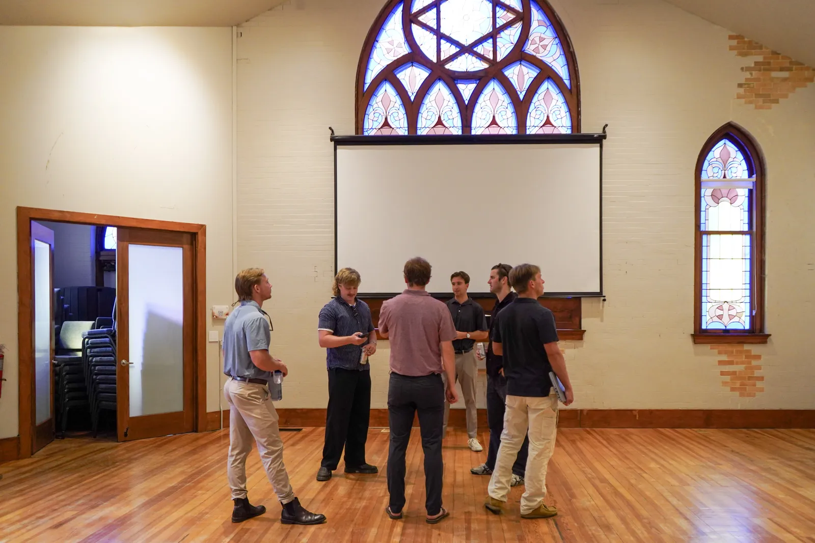 Professionals talk in a circle beneath the rose window and projection screen after a corporate gathering in the main hall