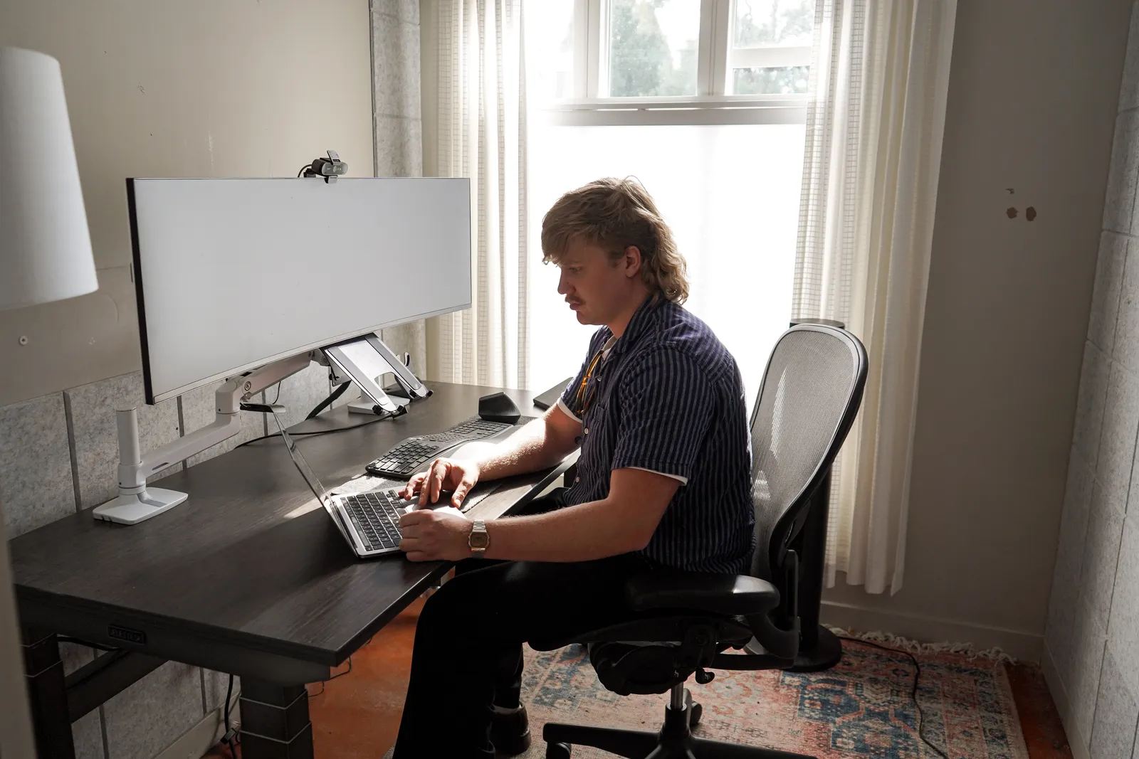 A member works at an ultrawide monitor in a sunlit private office at Merritt Workspace